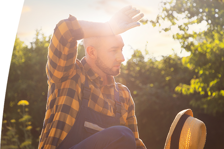 Summer heat. Portrait of a bearded adult gardener wiping sweat from his forehead. Gardening and Horticulture Concept.